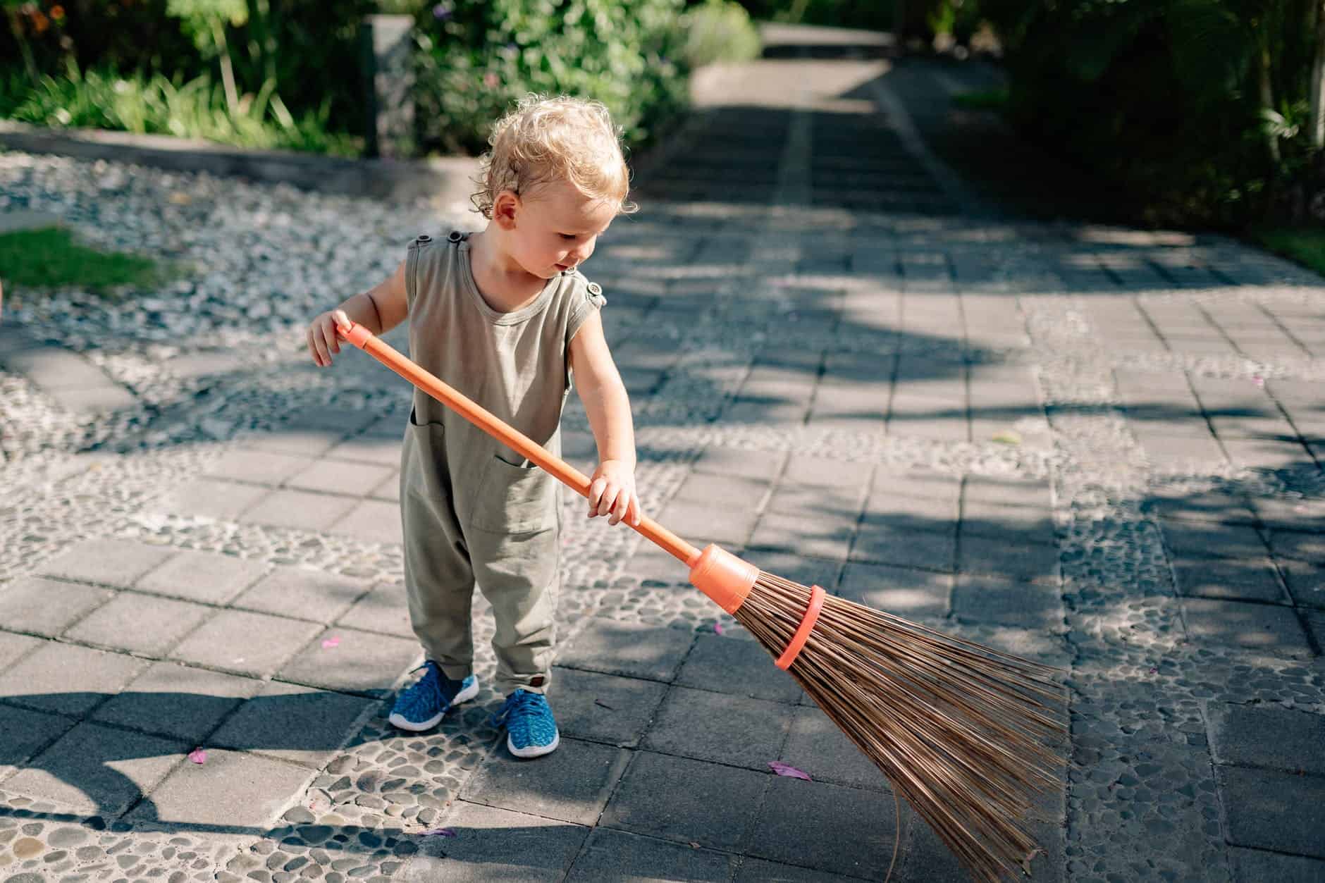 pexels-photo-4458033 charming child sweeping concrete pavement with broomstick