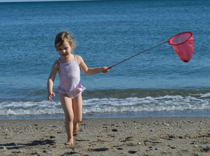 child playing with fishing net on sandy beach on holiday 