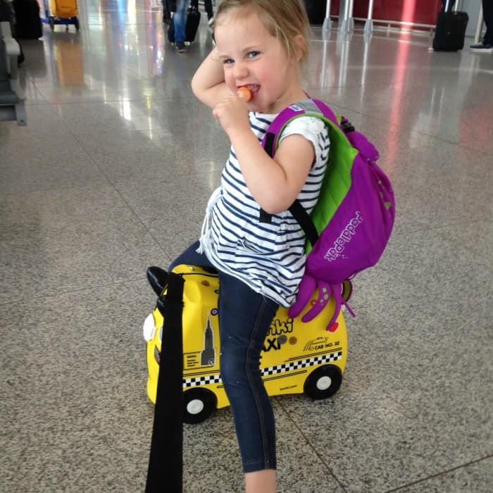 child sitting on suitcase with backpack 
