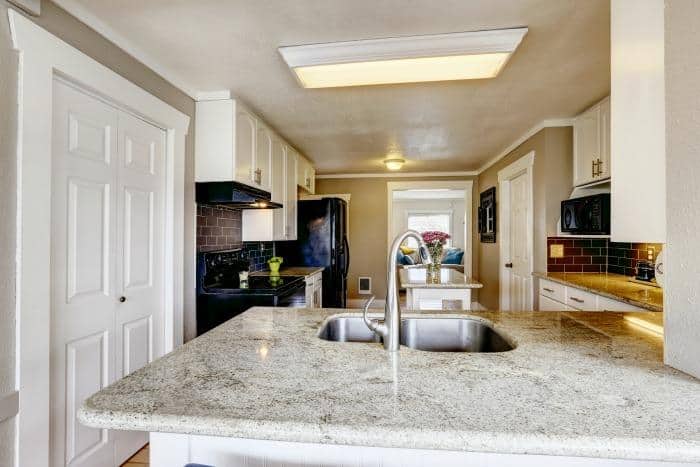 Kitchen cabinet with granite top and steel sink in kitchen room with brich tile back splash trim