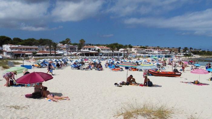 Punta Prima Beach with holiday makers on sunbeams with parasols 