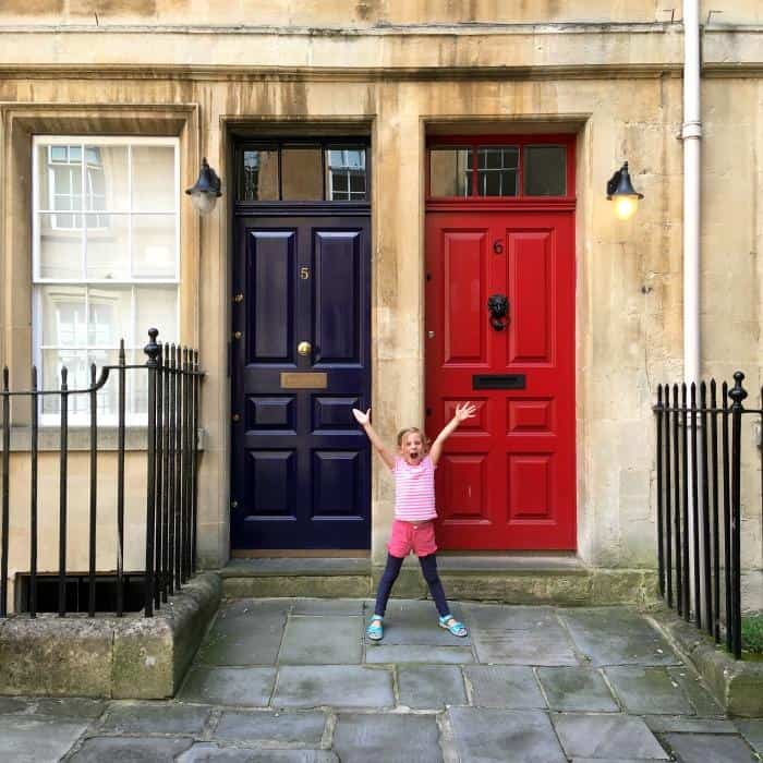 happy child stood in front of doors of typical houses and buildings found in Bath England