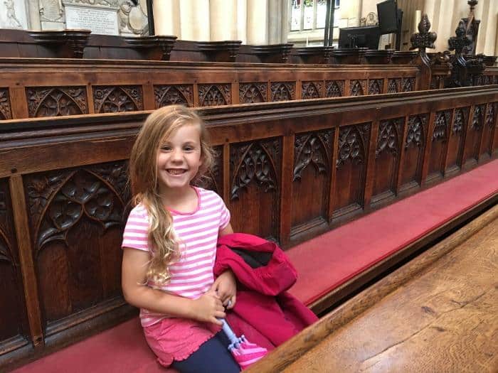 child sat on wooden pews inside Bath Abbey, England 