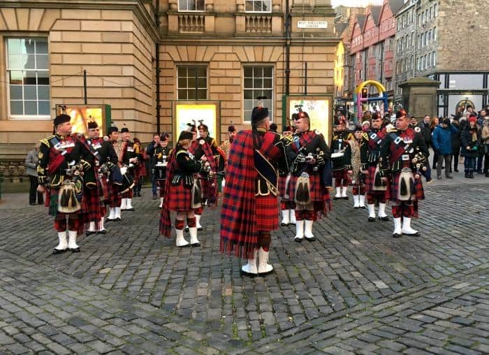a group of people playing bagpipes dressed in traditional kilts and uniform on Royal Mile in Edinburgh
