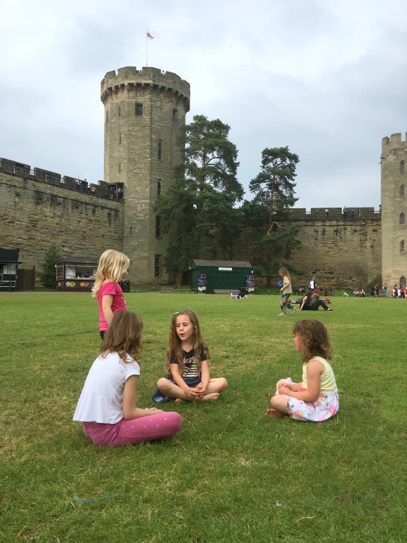 children sitting on grass inside warwick castle grounds 