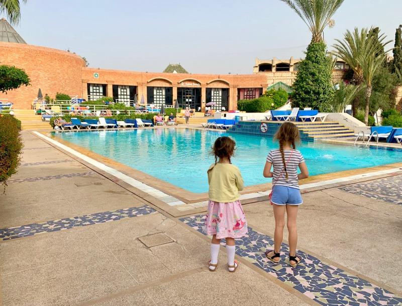two children stood by swimming pool looking at sun loungers and hotel restaurant
