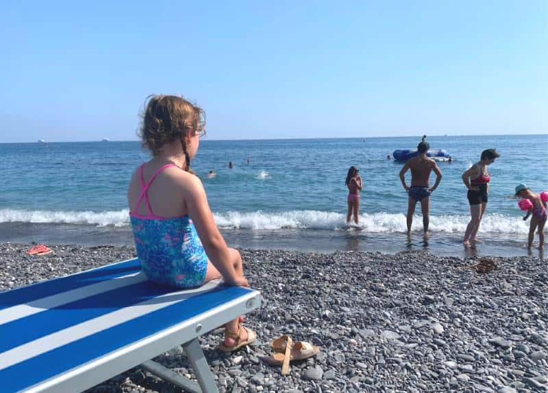 child sitting on beach looking out to sea in genoa