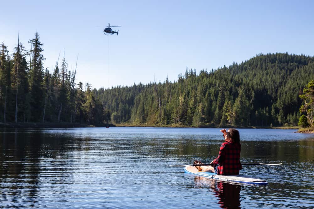  Girl on a paddle board is watching an helicopter fighting BC Wild Forest Fires.