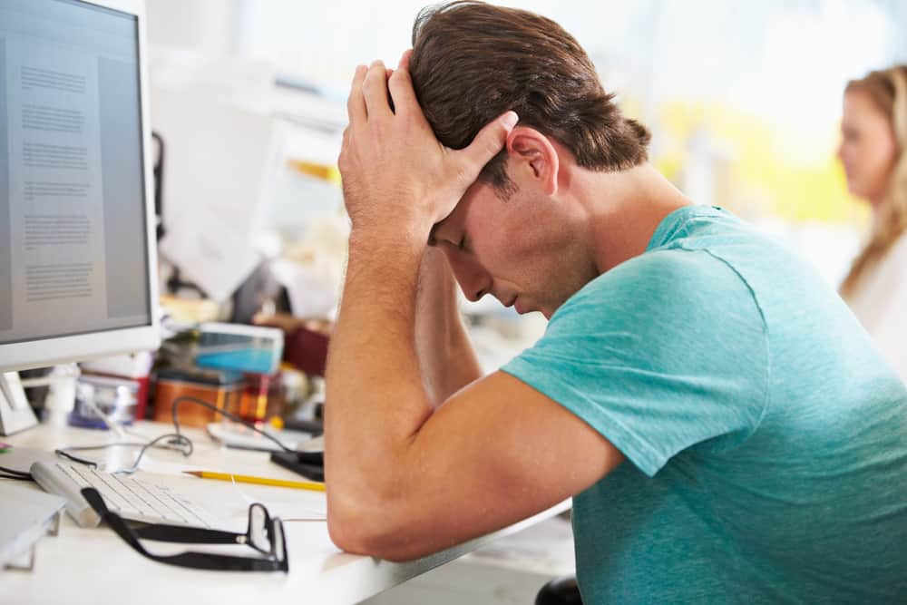 Stressed Man Working At Desk In Busy Creative Office