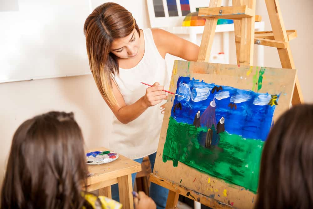 Pretty art teacher helping a student with her painting during art class