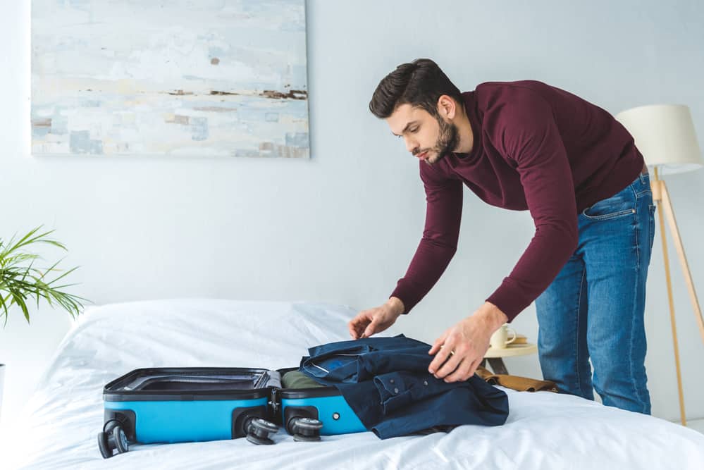 man packing suitcase on bed 