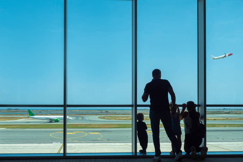 Airport. The family looks at the planes taking off. The family is waiting to Board the flight. View of the runway from the airport Windows. Organization of travel. Travel company.