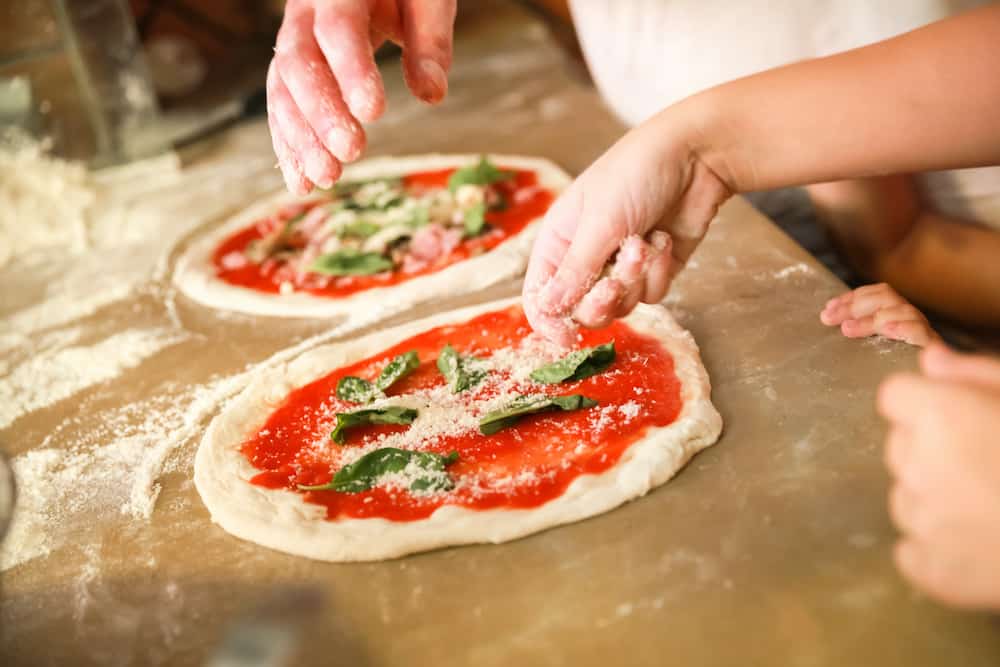 Preparing Classical Pizza Margherita. Cooks add grated parmesan cheese. Selective focus