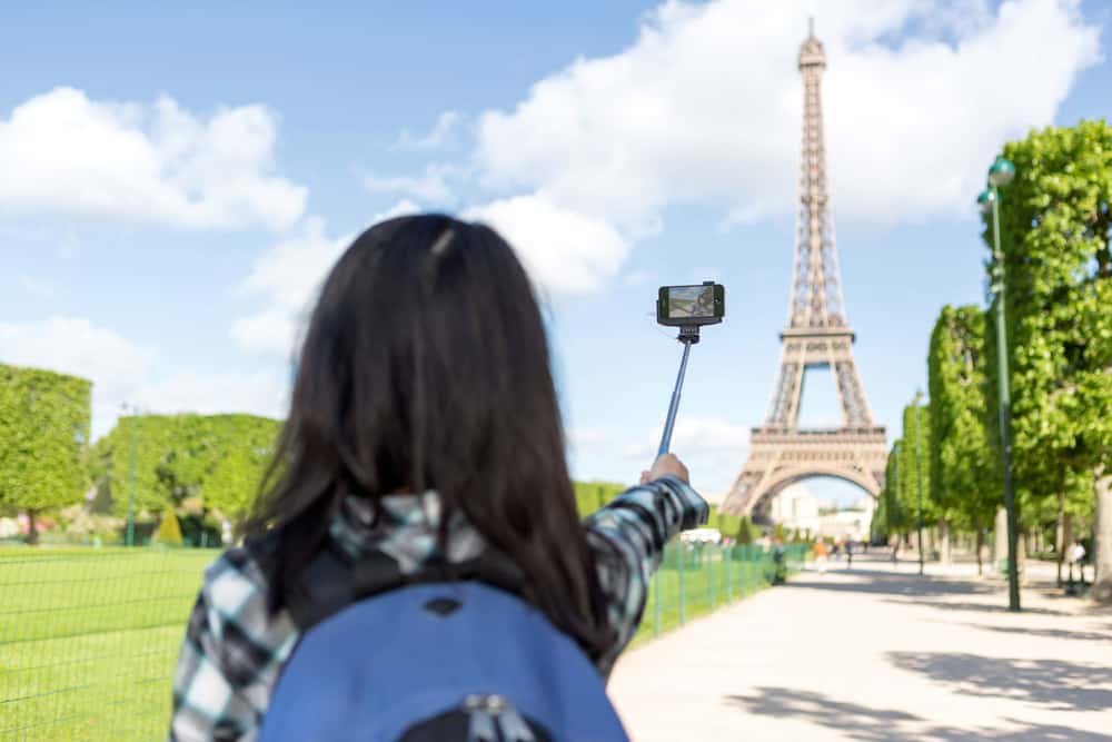 woman holding phone on selfie stick looking at Eiffel tower 