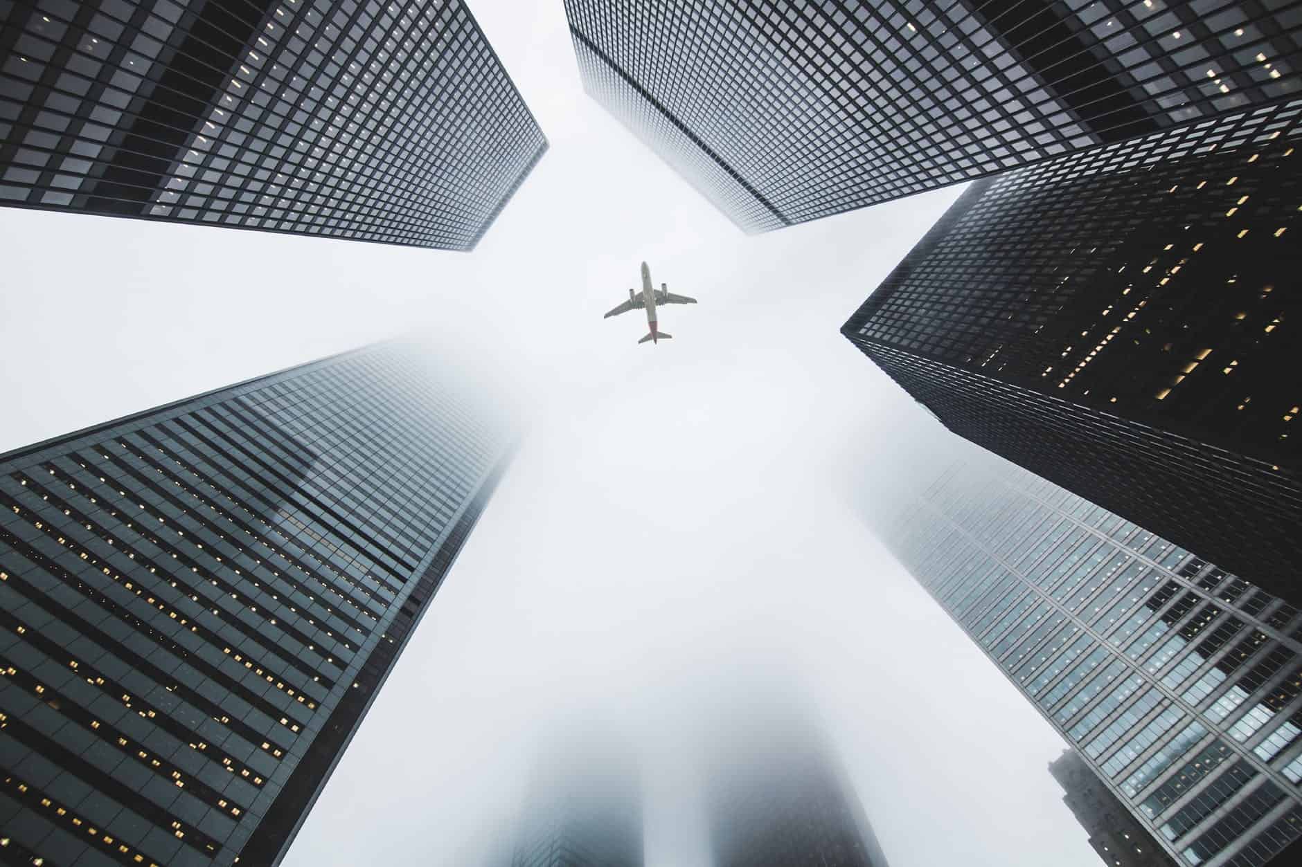 low angle photo of airplane flying over high rise buildings