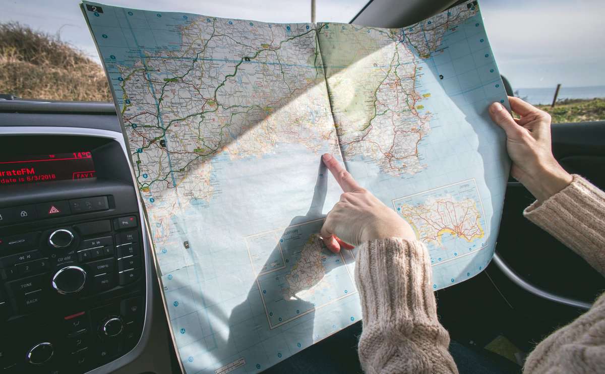 person wearing beige sweater holding map inside vehicle