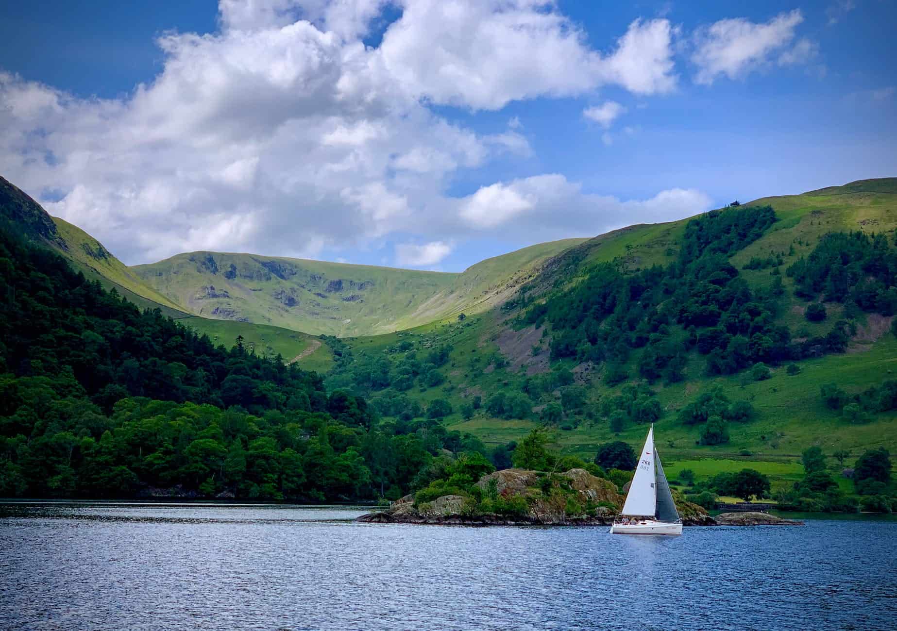 white sailboat on sea near green mountain under blue and white cloudy sky