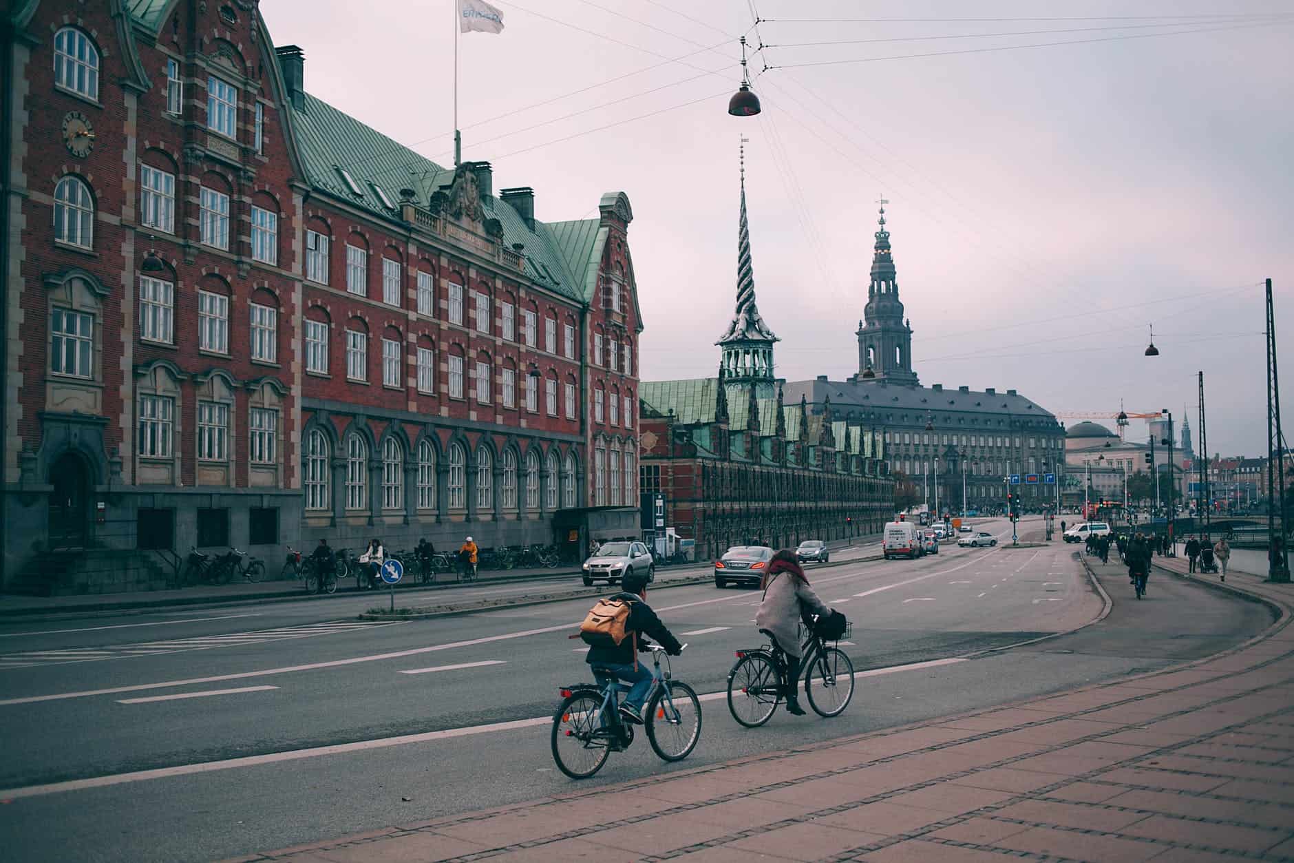 cyclists riding along wide embankment near historic buildings in city