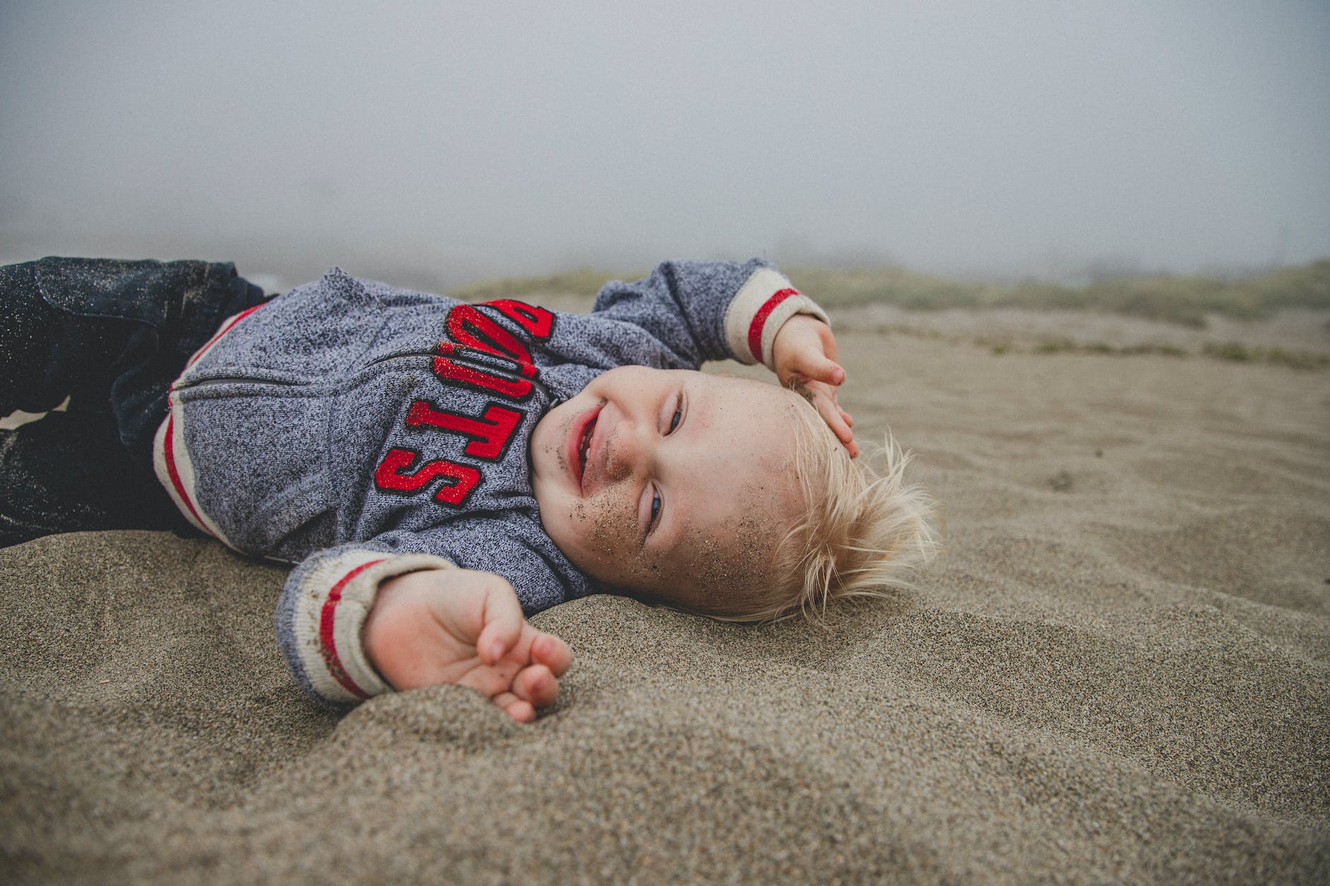 photo of boy lying on sand