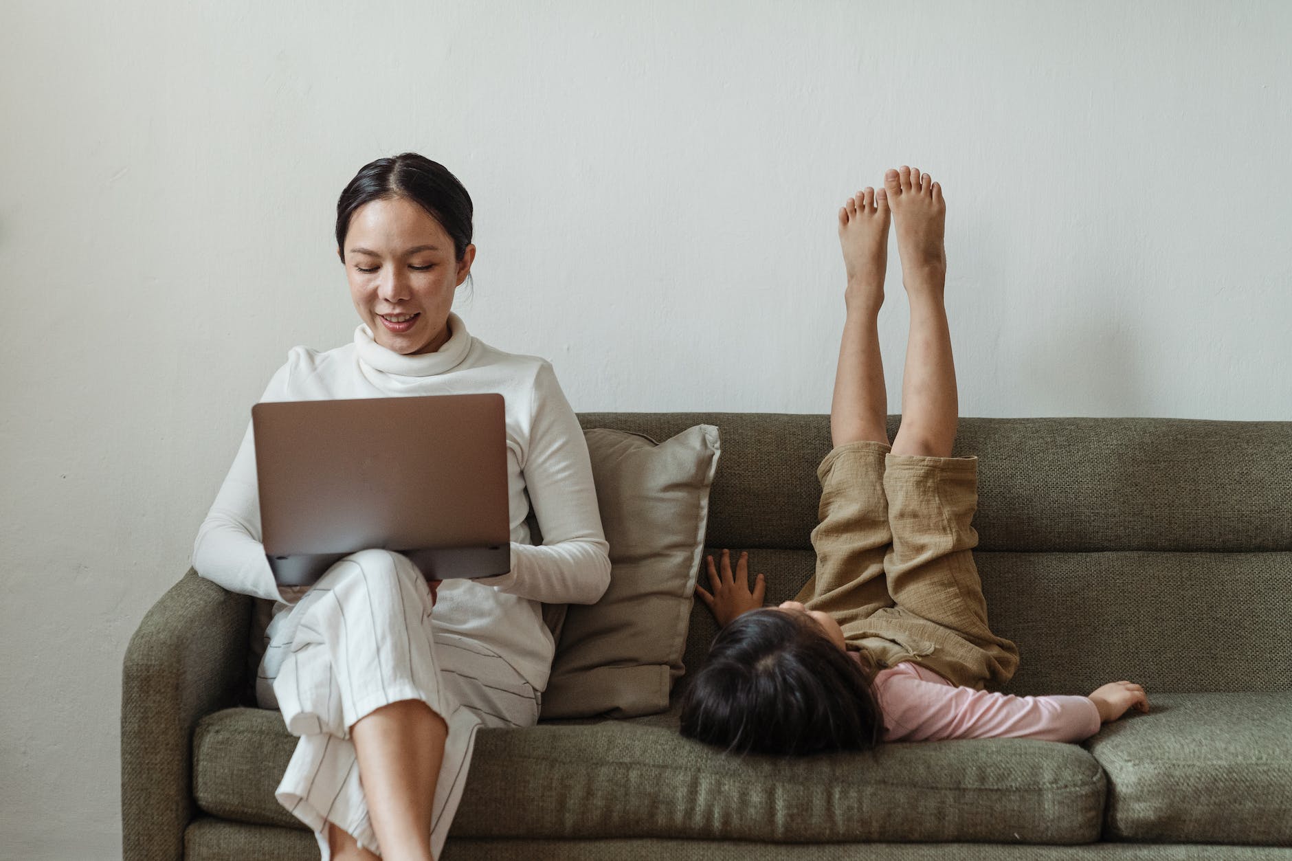 pexels-photo-4473899 cheerful mother working on laptop near daughter on couch