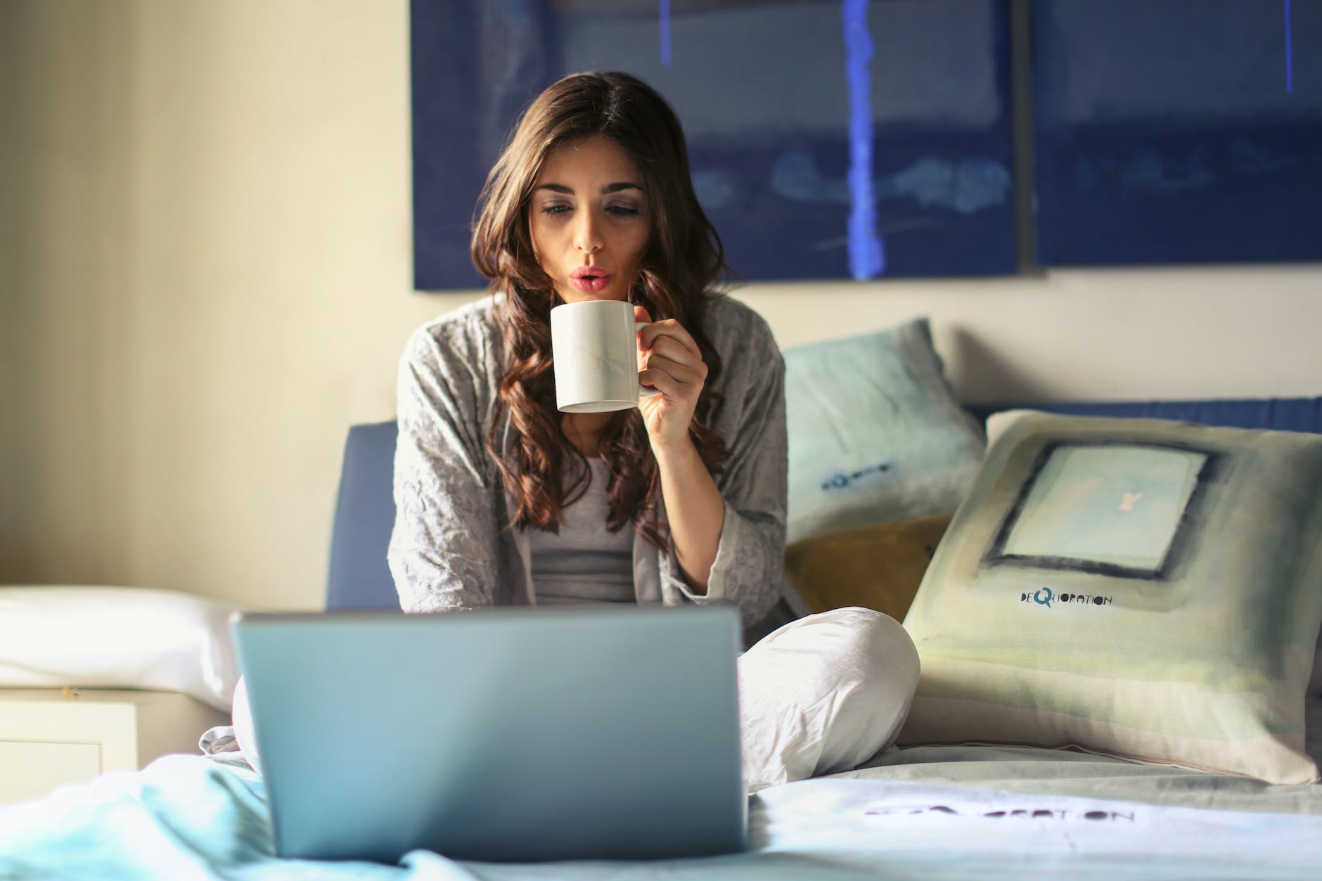 pexels-photo-935743 woman in grey jacket sits on bed uses grey laptop