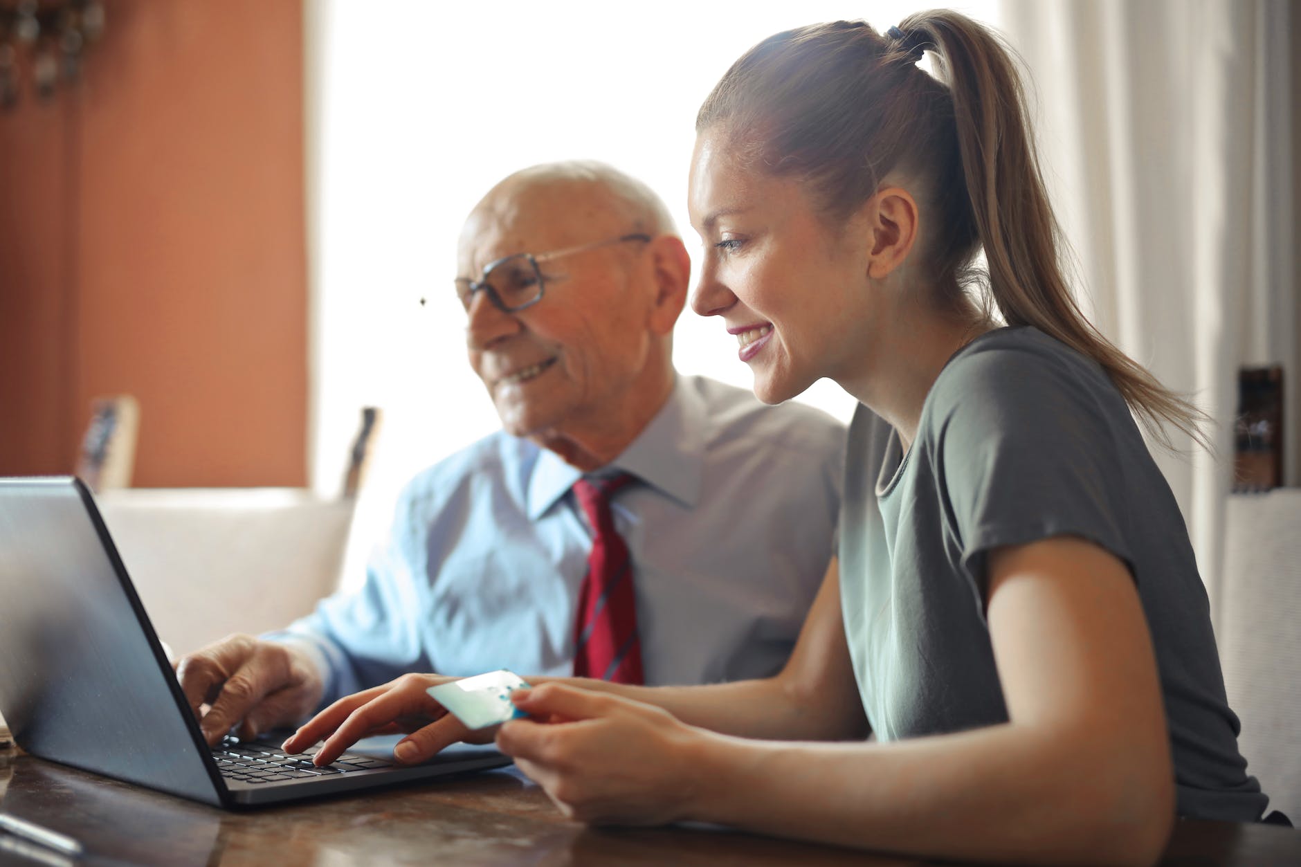 pexels-photo-3823488 young woman helping senior man with payment on internet using laptop