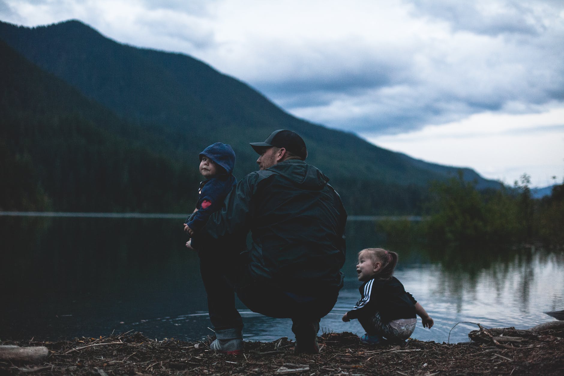 man with two kids near body of water