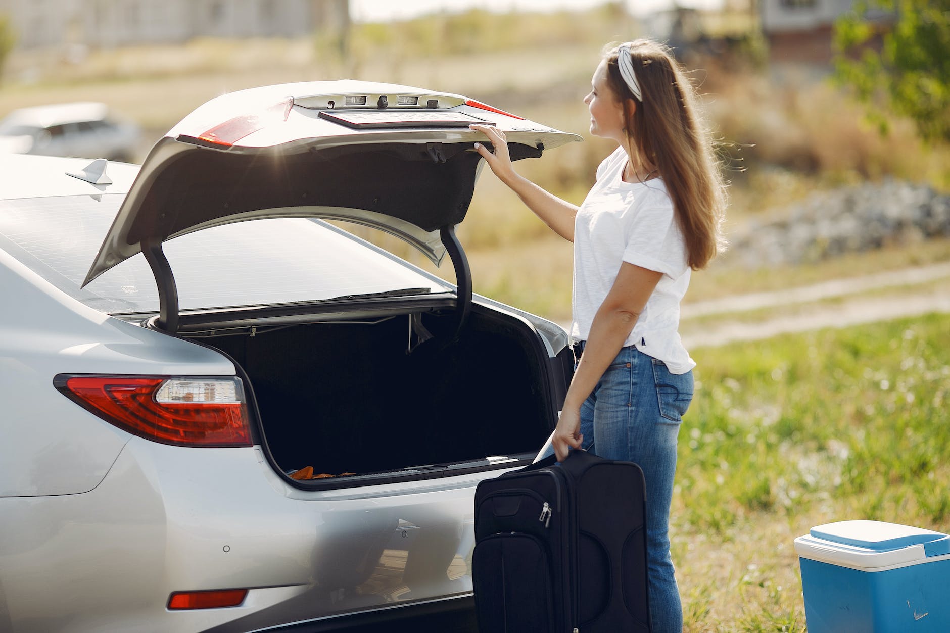 smiling young woman with luggage near automobile during car trip in nature