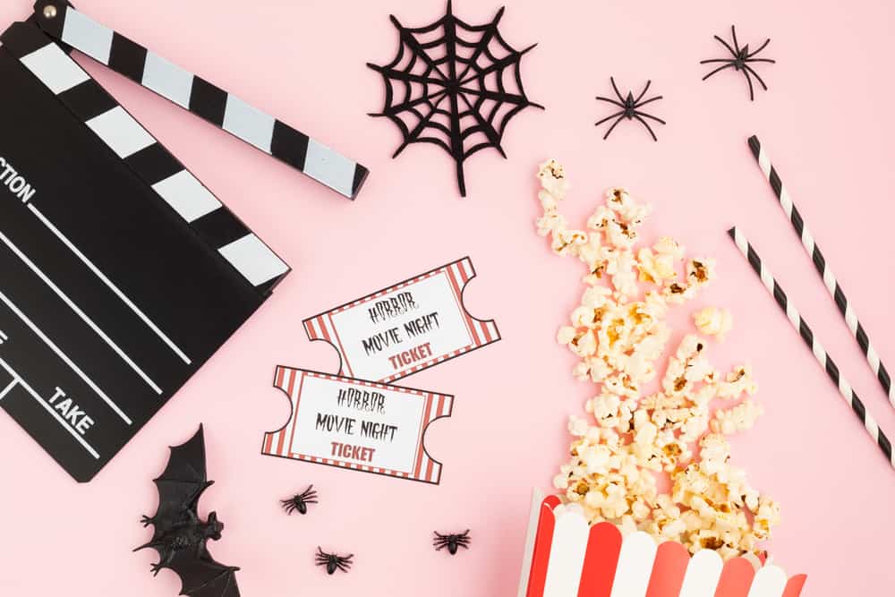 Movie clapperboard and halloween decoration over pink background. Horror movie night, halloween party invitation. Top view, copy space, mockup