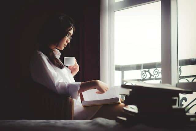 woman reading book and drinking tea in bedroom
