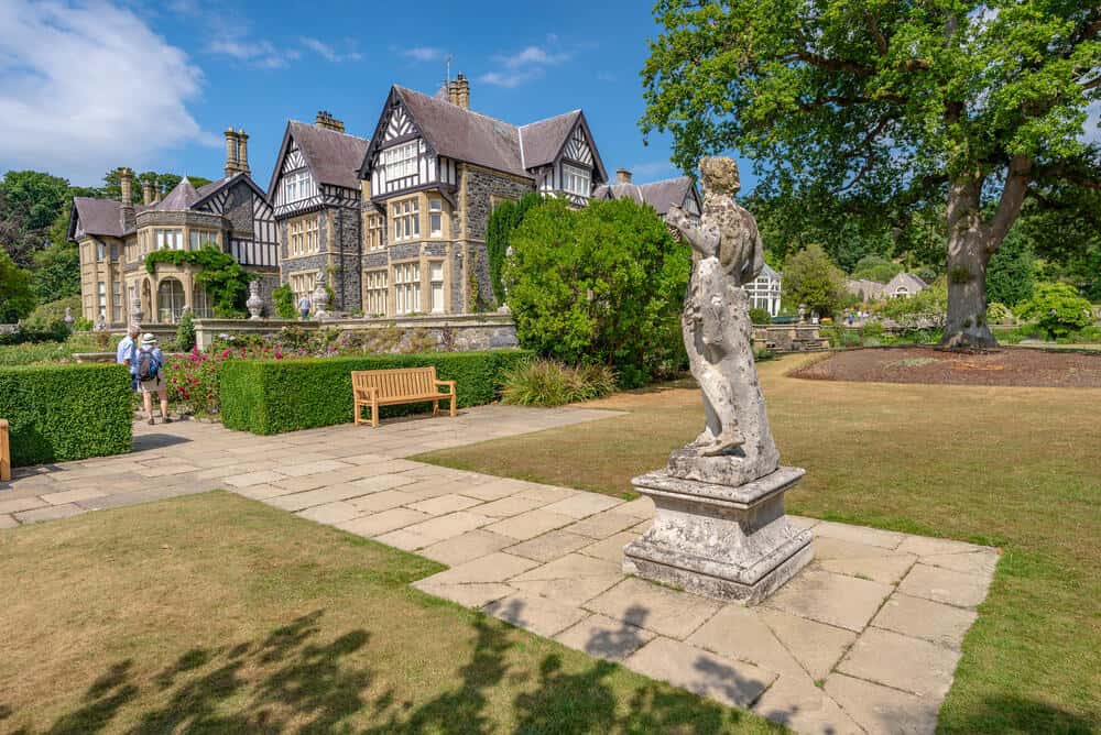 Classical statue looking towards Bodnant Hall and two visitors, Bodnant garden, Conwy, Wales, United Kingdom