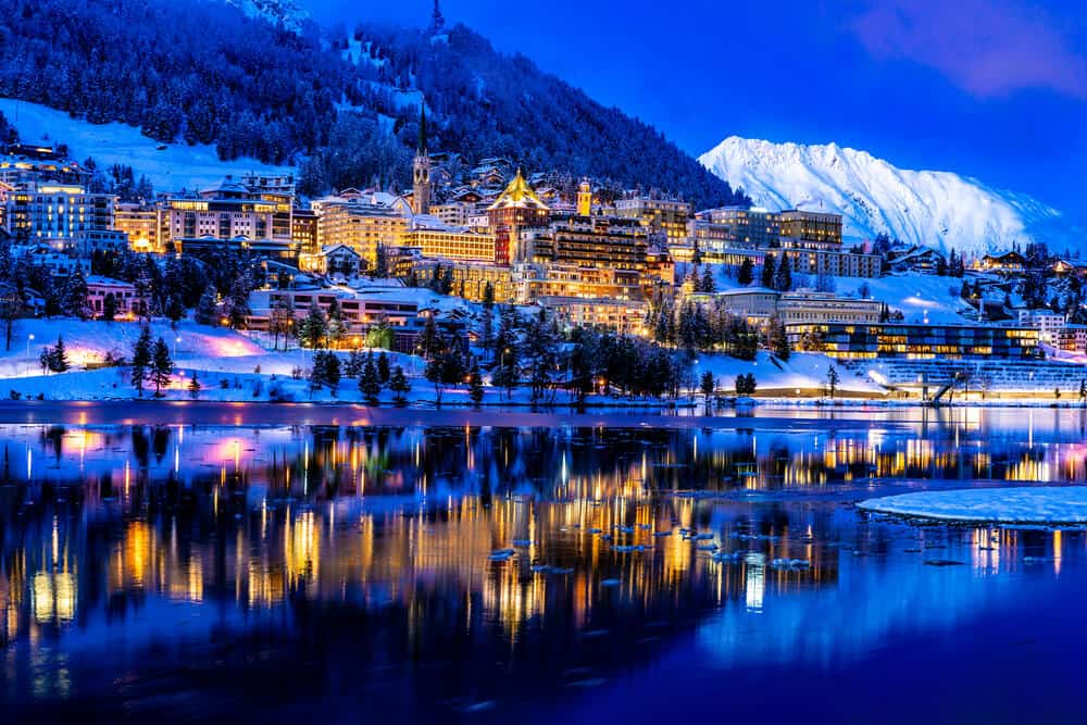 View of beautiful night lights of St. Moritz in Switzerland at night, with reflection from the lake and snow mountains in backgrouind