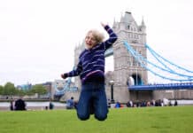 boy jumping on the lawn in front of beautiful Tower Bridge and River Thames on a sunny summer day, London, UK. Happy caucasian tourist kind enjoying view during family trip to England.