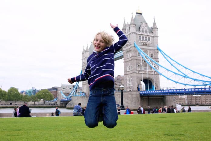boy jumping in front of london bridge boy jumping on the lawn in front of beautiful Tower Bridge and River Thames on a sunny summer day, London, UK. Happy caucasian tourist kind enjoying view during family trip to England.
