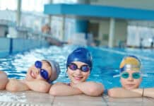 3 children at edge of pool with hats and googles on