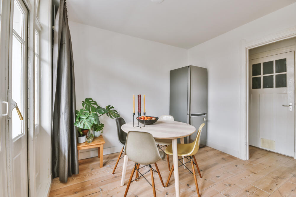 Wooden table with vase and chairs placed near opened balcony door in light dining room at home