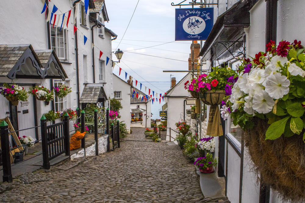 Cobbled street in Clovelly, North Devon, lined with whitewashed cottages, vibrant hanging flower baskets, and festive bunting overlooking the sea