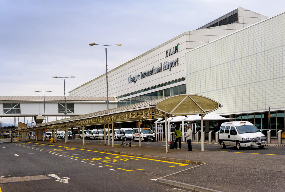 Exterior of Glasgow International Airport with taxi ranks, shuttle vans, and a covered passenger drop-off area, highlighting the airport’s accessible transport options and modern terminal design.