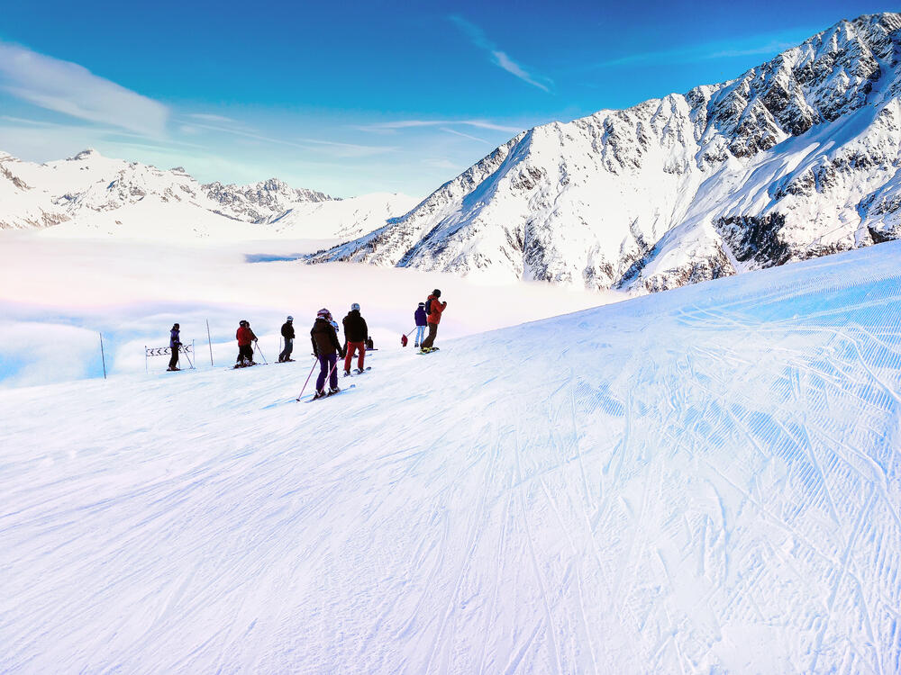 Skiers descending a pristine slope in Chamonix, France, with panoramic views of snow-covered peaks and a cloud-filled valley in the French Alps.