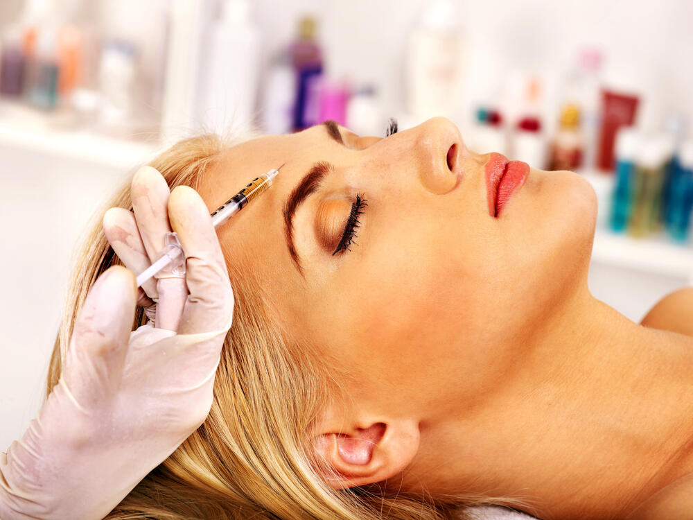 Close-up of a woman receiving a Botox injection in the forehead by a licensed professional wearing gloves at a cosmetic clinic for wrinkle treatment.