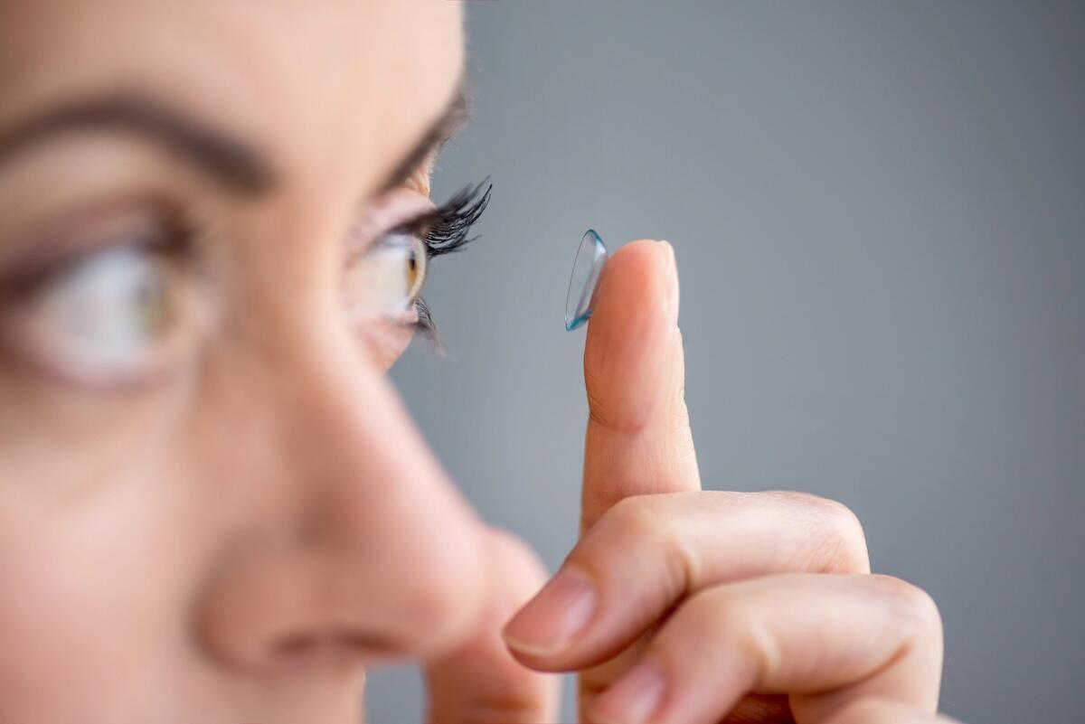 Close-up of a woman carefully inserting a contact lens onto her eye, demonstrating proper technique for first-time contact lens users.