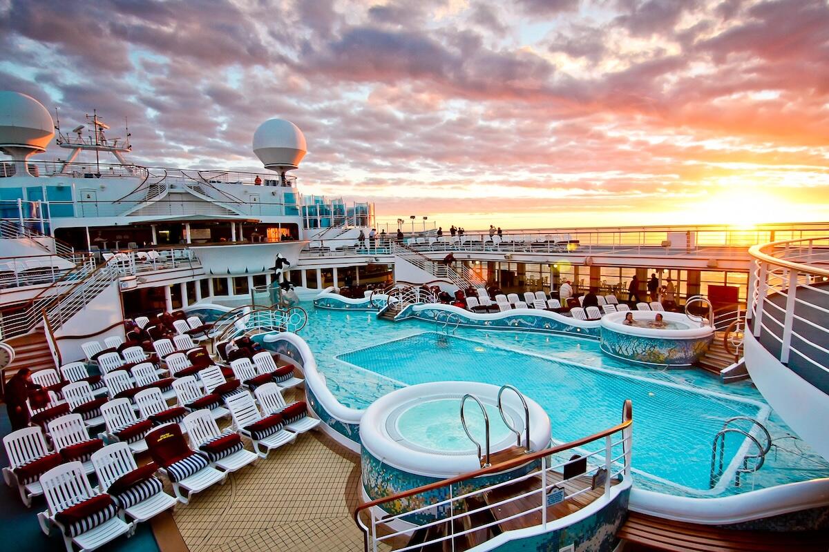 Sunset view from the pool deck of a cruise ship, featuring hot tubs, sun loungers, and a sparkling swimming pool — the perfect family-friendly setting for a relaxing mini cruise escape.